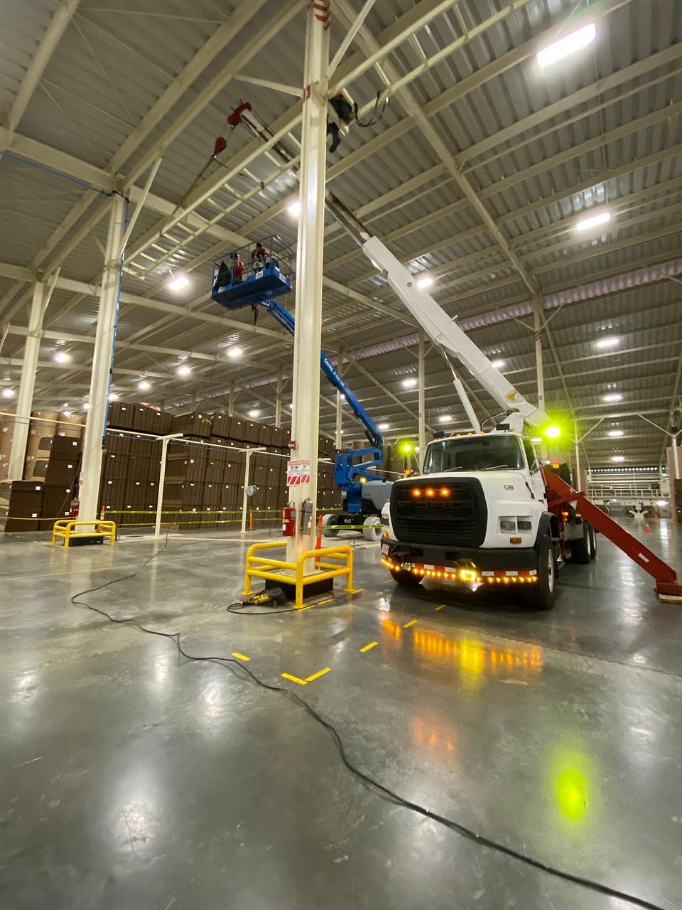 Camión canasta y plataforma elevadora trabajando de noche dentro de una bodega en operación