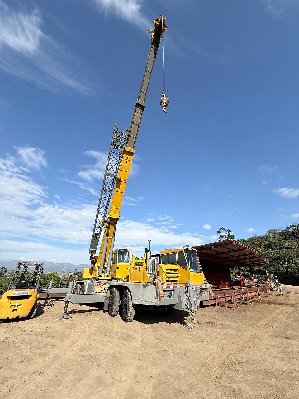 Grúa telescópica con el brazo extendido hacia el cielo, estacionada en un terreno de obra