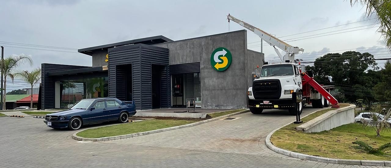 Camión grúa con el brazo levantado junto a un local comercial recién terminado