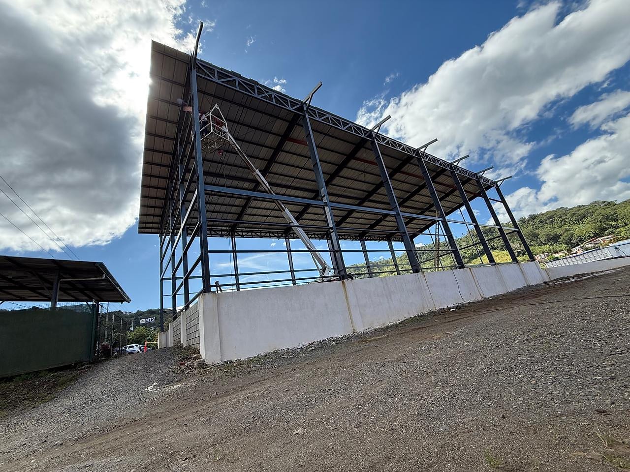 Nave metálica de un agua sobre muro de retención, vista desde abajo contra el cielo
