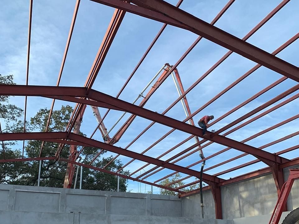 Cerchas de acero rojo a dos aguas montadas sobre paredes de concreto, vistas desde adentro
